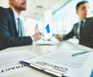 Business contracts on the desk with two male colleagues sitting on background